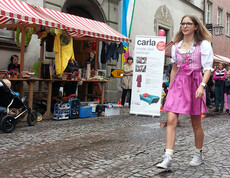 carla stellte anlässlich des Reuse Days zwei Stände in der feldkircher Innenstadt vor auf. Eine Fußgängerin mit pinkem Dirndl spaziert vorbei. 