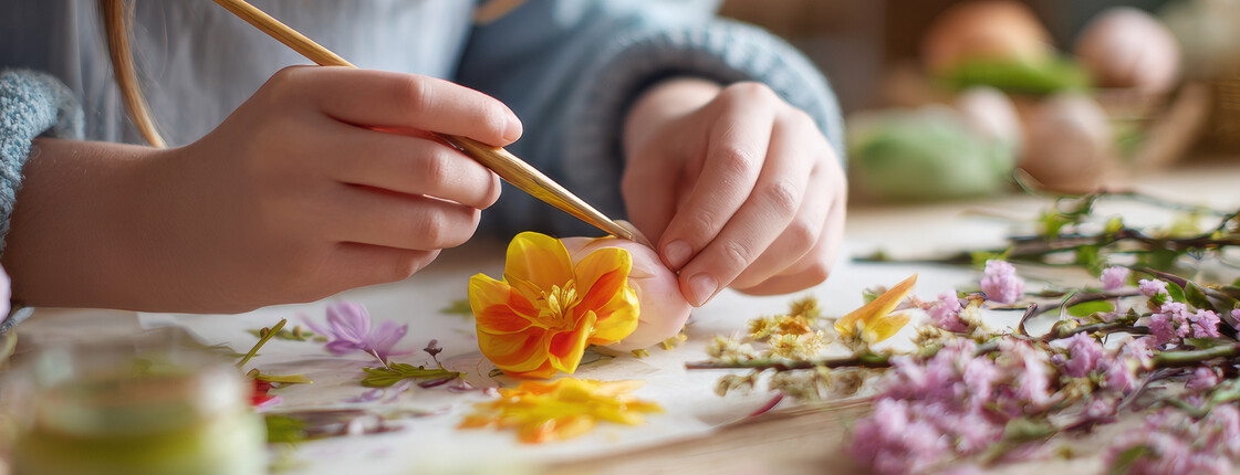 Hände gestalten mit Blüten und Pflanzen ein Kunstwerk aus Naturmaterialien.