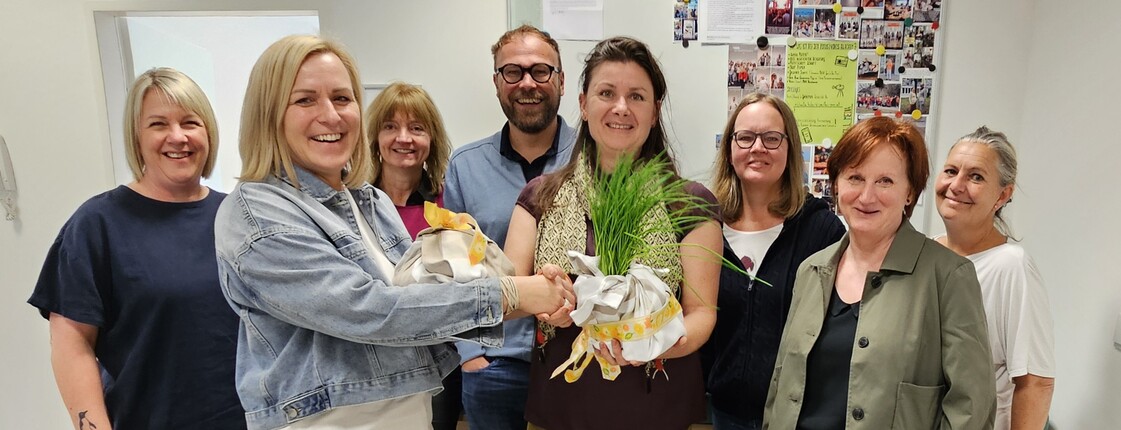 Eine Gruppe von Erwachsenen steht beisammen und schaut in die Kamera, Geschenke werden überreicht.
