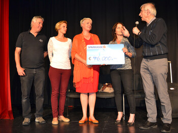 Fünf Menschen stehen auf einer Bühne für eine Scheckübergabe.