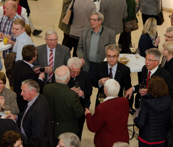 Personen stehen zusammen und trinken ein Glas Wein