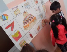 Zwei Kindergartenkinder stehen vor einem selbstgemalten Plakat, dass ungesunde Lebensmittel zeigt.