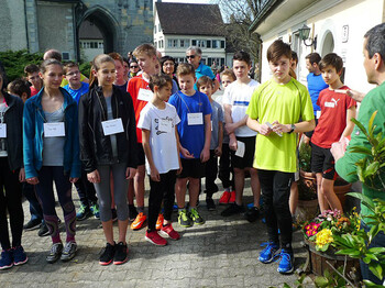 Mehrere Menschen stehen hintereinander aufgestellt. Alle tragen Sportkleidung und schauen in die Richtung eines Mannes, der etwas erklärt.