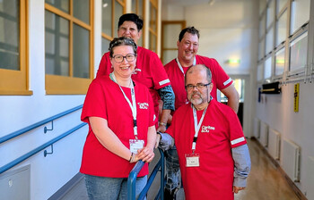 Vier Personen in roten Caritas-T-Shirts stehen gemeinsam im Flur und engagieren sich im inklusiven Projekt.