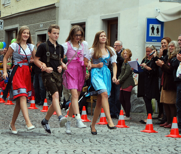 Drei junge Erwachsene und ein junger Erwachsener gehen Hand in Hand in Tracht am carla Reuse Day durch die Innenstadt. Die drei Frauen tragen jeweils bunte Dirndl und der junge Herr klassisch Lederhosen. 