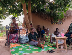 Mehrere Erwachsene im Südsudan sitzen vor einer Lehmhütte.