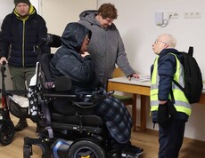 Eine Person im Rollstuhl und drei weitere in einem neuen Haus.