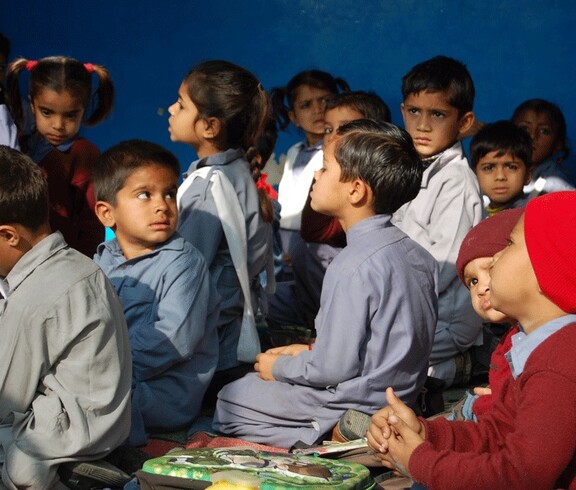 Eine Gruppe von Kindern in Schulkleidung schaut aufmerksam in eine Richtung, im Hintergrund eine blaue Wand.