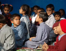 Eine Gruppe von Kindern in Schulkleidung schaut aufmerksam in eine Richtung, im Hintergrund eine blaue Wand.