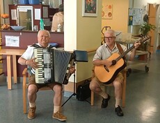 Zwei Personen sitzen in einem Aufenthaltsbereich eines Pflegewohnhauses und sorgen mit Akkordeon und Gitarre für musikalische Unterhaltung.