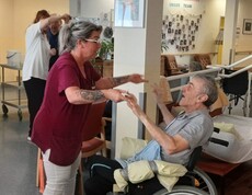 Eine Pflegekraft tanzt mit einem Bewohner im Rollstuhl und sorgt gemeinsam mit weiteren Personen im Hintergrund für eine fröhliche Atmosphäre beim „Tanz in den Mai“ im Pflegewohnhaus.