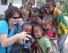 Caritas-Mitarbeiterin Elke Kager zeigt äthiopischen Kindern Fotos auf ihrer Kamera. Die Kinder schauen gespannt und sind erfreut. Elke trägt eine blaue Bluse und die Kinder sind bunt, in unterschiedlichen Farben gekleidet. 