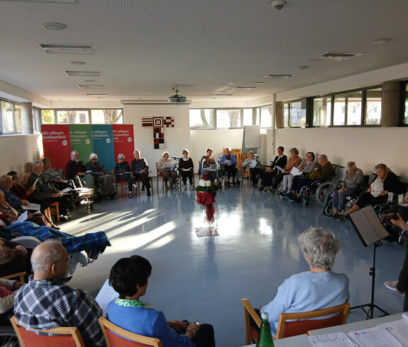 Bewohner*innen sitzen im Kreis, Adventkranz auf rotem Tuch in der Mitte