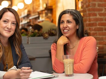 Vier Frauen in Business Kleidung sitzen in einem Café und unterhalten sich.