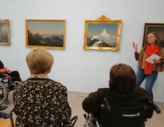 Gruppe von Bewohner*innen sitzt vor Gemälden im Museum, während eine Vermittlungsperson Kunstwerke erklärt