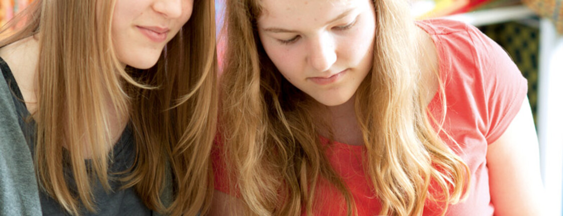 Zwei Mädchen mit langen blonden Haaren sind gerade am Nähen. Das eine trägt ein grünes Obertreil, das andere ein rotes. Symbolbild für die Startbahn von carla Vorarlberg und Jugendlichen bzw. jungen Menschen, die bei carla eine temporäre Arbeit gefunden haben