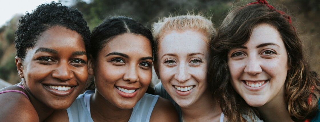 Vier Freundinnen stehen im Freien zu einem Gruppenfoto zusammen.