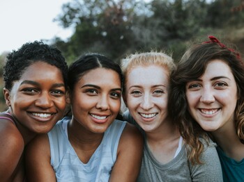 Vier Freundinnen stehen im Freien zu einem Gruppenfoto zusammen.