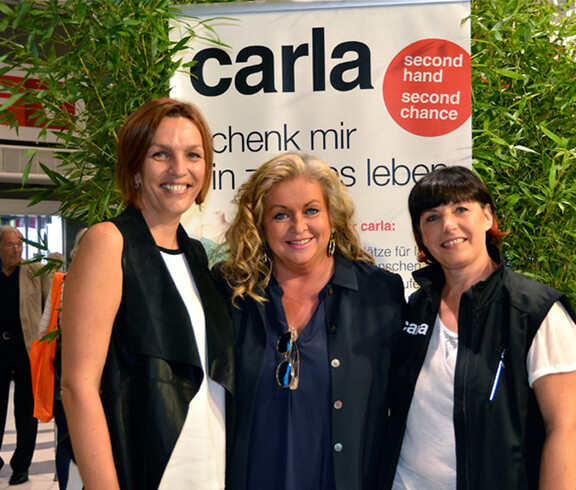 Drei Frauen mittleren Alters stehen vor einem Carla Plakat. 