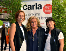 Drei Frauen mittleren Alters stehen vor einem Carla Plakat. 