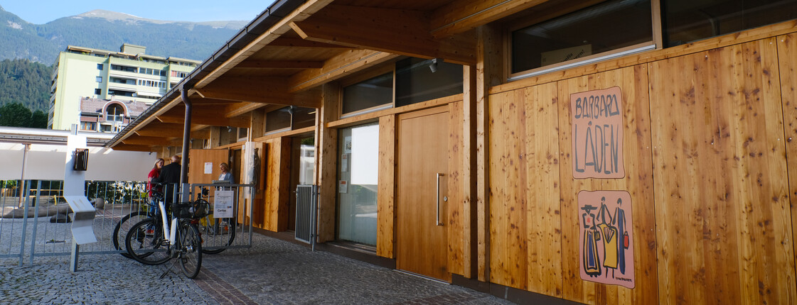 Zwei Personen stehen vor einem mit Holz verkleideten Gebäude und unterhalten sich.