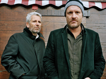 Zwei Herren mittleren Alters schauen streng in die Kamera.