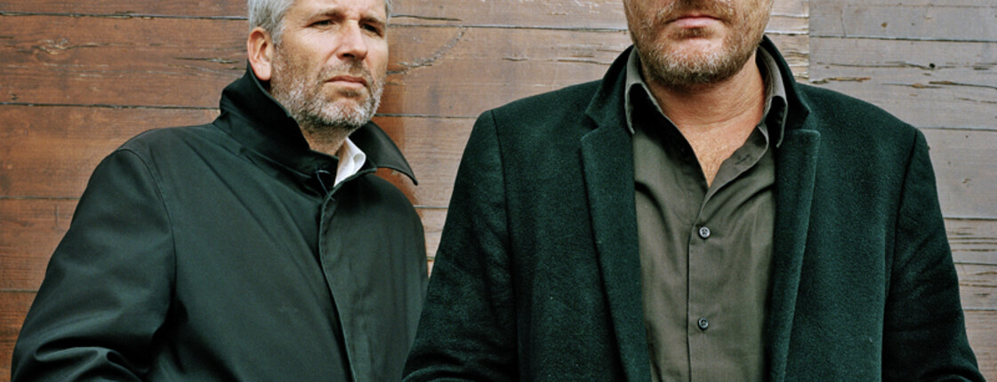 Zwei Herren mittleren Alters schauen streng in die Kamera.