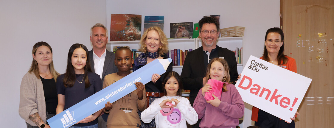 Gruppe von Kindern und Erwachsenen im Lerncafé Don Bosco Klagenfurt hält Spendenzeichen von Wietersdorfer und „Danke“.