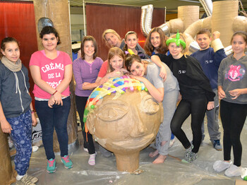 Jugendliche und eine Erwachsene Frau stellen sich um einen selbstgebastelten überdemensionierten Kopf. Sie sind in einem Raum und tragen Alltagskleidung. 