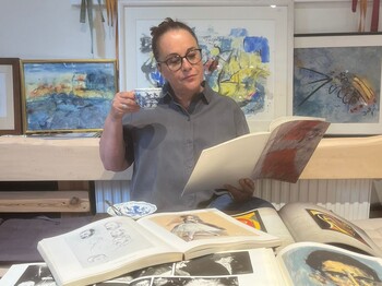 Frau mit Brille hält eine Kaffeetasse und ein Kunstbuch in den Händen.