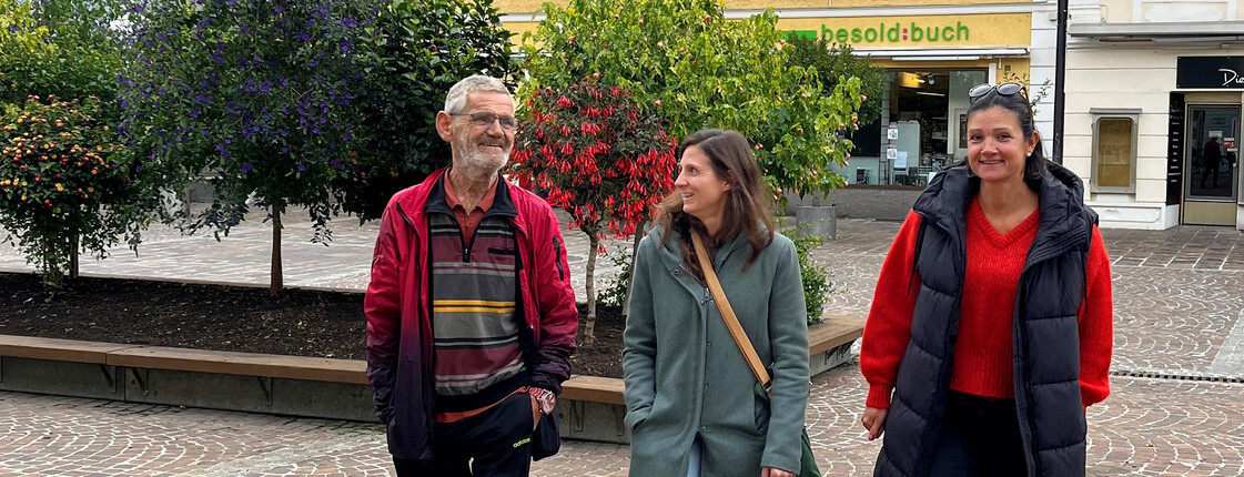 Drei Personen spazieren plaudernd beim gemeinsamen Spazierengehen.