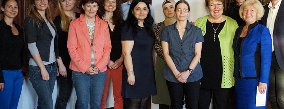 Einige Teilnehmer*innen der Integrationsgespräche der Caritas sind in einem Raum versammeln und posieren vor einem Banner der Caritas.