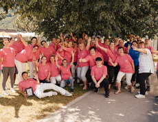 Große Gruppe von Mitarbeitenden in pinken Shirts posiert im Garten unter einem Baum beim Sommerfest