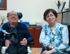 Ein lächelnder Mann im Rollstuhl sitzt neben einer Frau in einem Büro – beide wirken freundlich und offen.