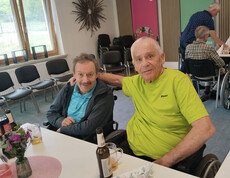 Zwei Bewohner sitzen bei Getränken an einem Tisch, eine Person legt den Arm um die andere während der Muttertagsfeier.