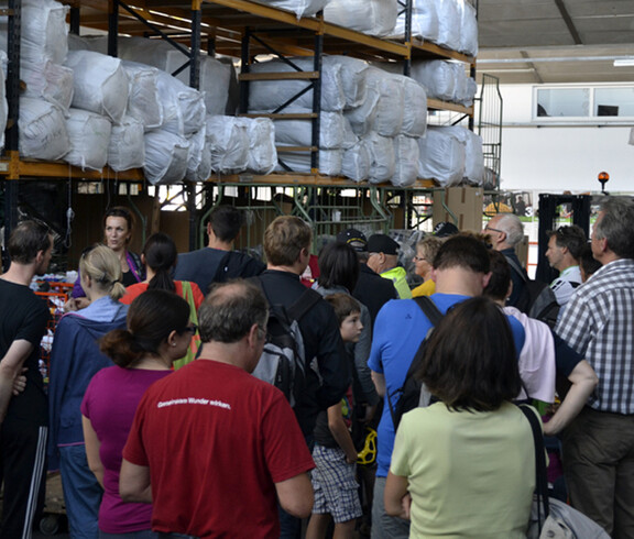 Eine Menschenmenge von ca. 30 Personen steht eng zusammen im carla Kleidersortierwerk. 