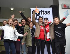 Kinder und Jugendliche stehen vor der Sparkasse in Feldkirch, jubeln und strecken ihre Hände in die Luft. Im Hintergrund befindet sich ein Caritas Roll-Up. Sie nahmen bei einem Laufwettbewerb teil. Manche tragen gemeinsame Trikots. Alle wirken freundlich und die Stimmung ist ausgelassen. 