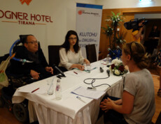 Ein Mann im Rollstuhl und zwei Frauen nehmen an einer Pressekonferenz von Caritas Albanien im Hotel Rogner in Tirana teil.