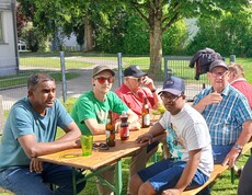 Viele Menschen sitzen an Bierbänken im Garten