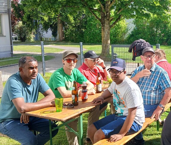 Viele Menschen sitzen an Bierbänken im Garten