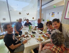 Ein großer Tisch voller Bewohnerinnen und Bewohner, Angehöriger und Mitarbeitender bildet beim Sommerfest im Pflegewohnhaus den Mittelpunkt eines gemeinsamen Essens in freundlicher und festlicher Umgebung.