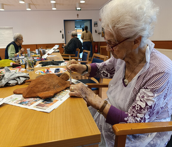 Bewohnerin trägt mit Pinsel Farbe auf eine Papiermaché-Schildkröte auf, am Tisch liegen Farben und Material.