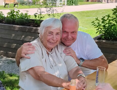 Zwei Personen sitzen eng beieinander an einem Tisch im Garten des Pflegewohnhauses während des Grillfests.