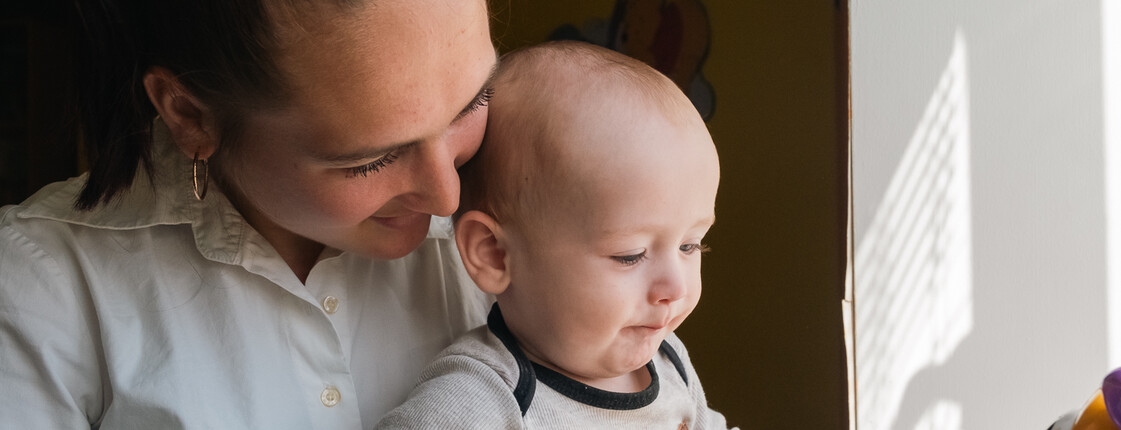 Eine junge Mutter hält ihr kleines Baby liebevoll in den Armen und lächelt ihm zu.