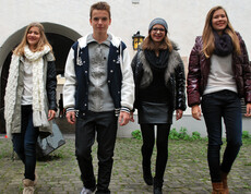 Drei junge Erwachsene und ein junger Erwachsener sind modisch, dunkel gekleidet. Aufgenommen wurde das Bild in einem Innenhof. 