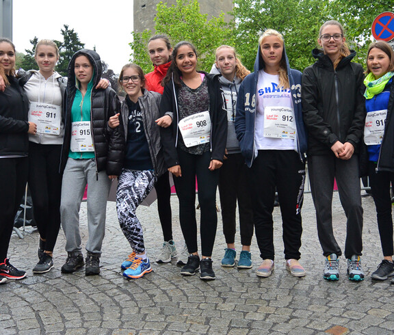 Um die zehn weibliche Jugendliche stehen in der feldkicher Innenstadt bei der Sparkasse zu einem Gruppenfoto zusammen. Sie tragen größtenteils dunkle Kleidung und umarmen sich mitunter gegenseitig. 