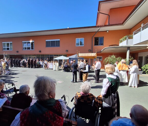 Vor dem Pflegewohnhaus versammelt sich eine große Prozession mit Kindern und Gottesdienstgestaltung, um gemeinsam eine feierliche Andacht im Freien zu feiern.