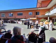 Vor dem Pflegewohnhaus versammelt sich eine große Prozession mit Kindern und Gottesdienstgestaltung, um gemeinsam eine feierliche Andacht im Freien zu feiern.