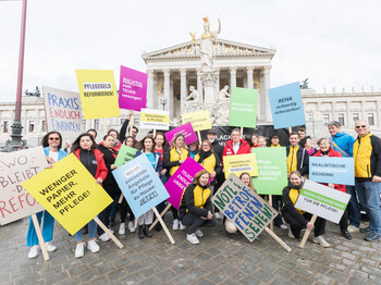 Mitglieder von Caritas, Diakonie, Hilfswerk, Rotes Kreuz und Volkshilfe mit bunten Tafeln vor dem Parlament