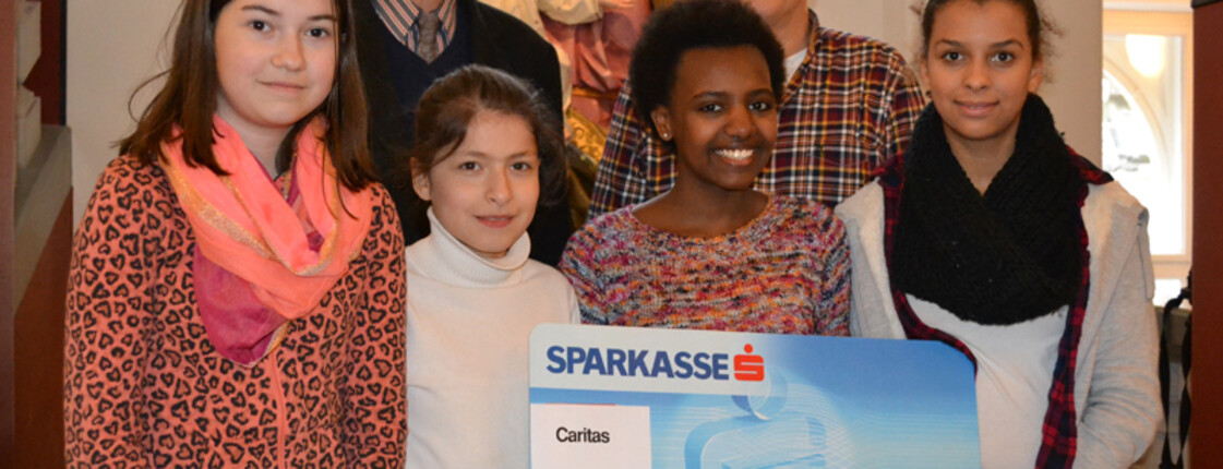 Caritas-Seelsorger Elmar Simma mit Kindern unterschiedlicher Nationalitäten. Sie zeigen einen Check im Wert von 1000 Euro. 
